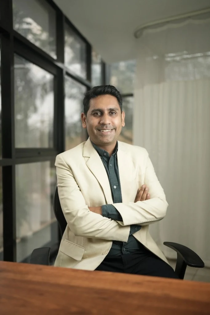 Professional portrait of Dr. Kundan Kharde wearing a cream blazer, sitting in an office setting with arms crossed.