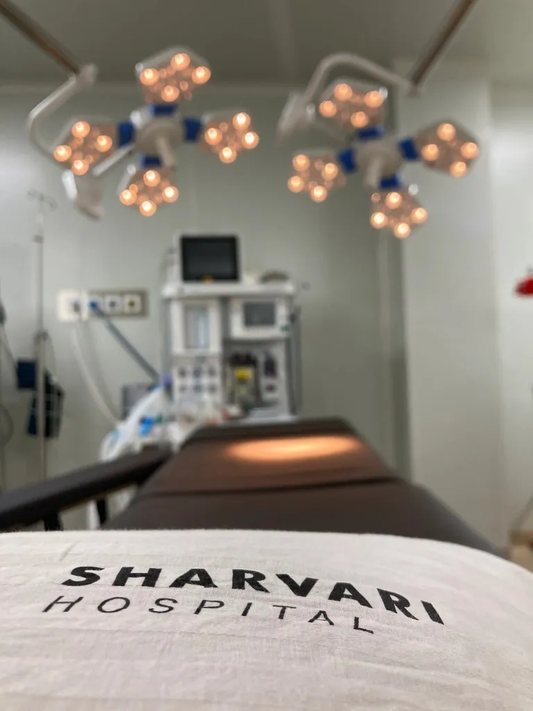 Surgical suite at Sharvari Hospital showing overhead LED lights, monitoring equipment, and Sharvari Hospital branding on the operating table.